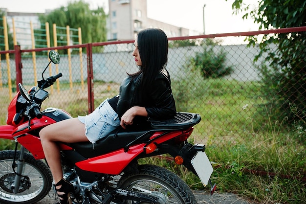 Portret van een coole en geweldige vrouw in jurk en zwart leren jack zittend op een coole rode motor