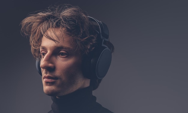 Portret van een creatieve sensuele man in een zwarte trui die muziek luistert met een koptelefoon.