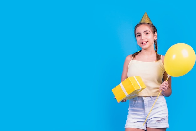 Portret van een de giftdoos en ballons van de meisjesholding in haar hand op blauwe oppervlakte