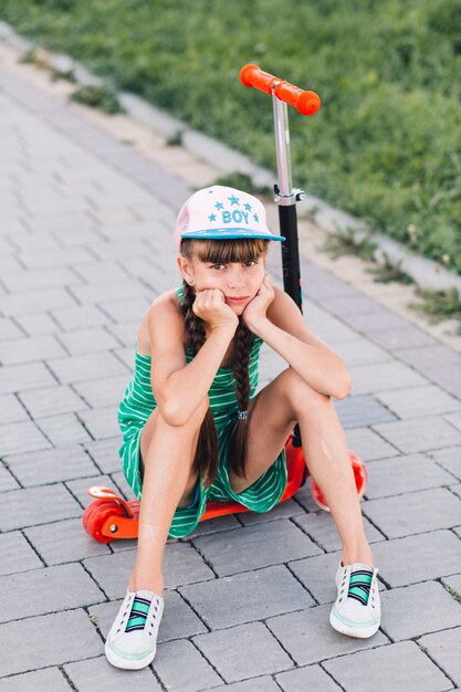 Portret van een droevig meisje die glb-zitting op rode duwautoped dragen