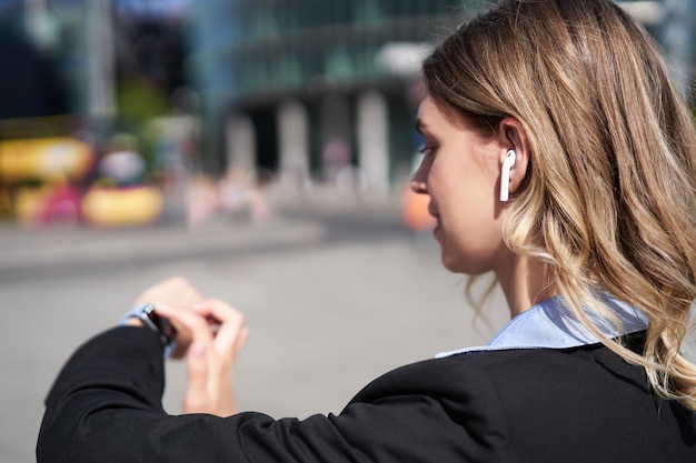 Gratis foto portret van een drukke zakelijke vrouw in een draadloze koptelefoon die naar de tijd kijkt bij het inchecken van haar digitale horloge