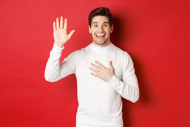 Portret van een eerlijke glimlachende man in een witte trui die een belofte doet en zweert de waarheid te vertellen...