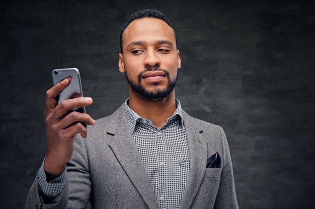 Portret van een elegante, bebaarde zwarte Amerikaanse man in een grijs pak houdt een smartphone vast.