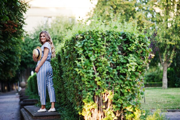 Portret van een fantastische jonge vrouw in gestreepte overall die op de slagboom in het park loopt