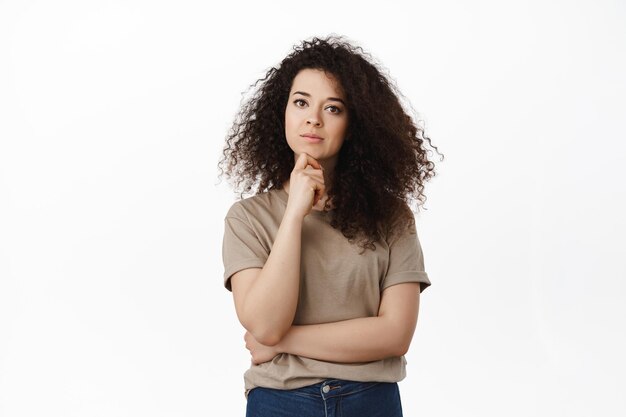 Portret van een gecompliceerde vrouw die een besluit neemt, nadenkt en serieus naar de camera kijkt, nadenkt over de keuze, bedachtzaam staat tegen een witte achtergrond