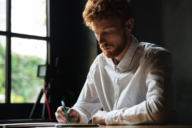 Portret van een geconcentreerde roodharige man schrijven in een notitieblok