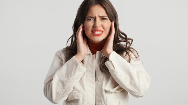 Portret van een geërgerd brunette meisje dat emotioneel oren bedekt met handen over grijze achtergrond Zo luide uitdrukking