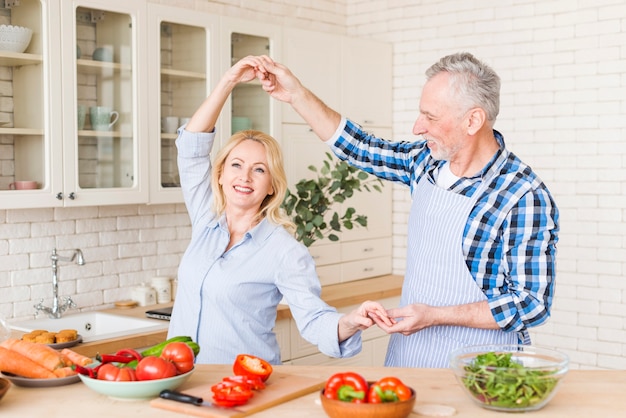 Portret van een gelukkig hoger paar die in de keuken dansen