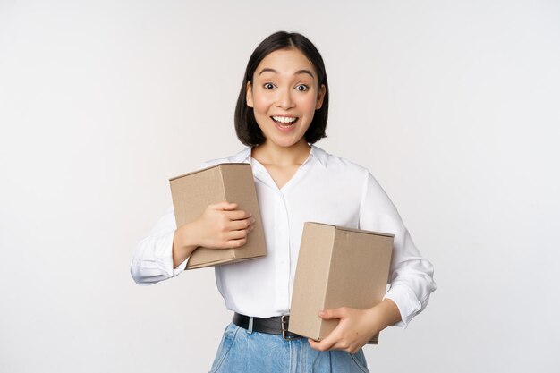 Portret van een gelukkig Koreaans meisje dat twee dozen vasthoudt en glimlachend kijkt verbaasd naar het cameraconcept van winkelen op een witte achtergrond