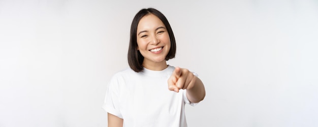 Portret van een gelukkig lachende aziatische vrouw met witte tanden die met de vinger naar de camera wijst en ervoor kiest om je te feliciteren over een witte achtergrond