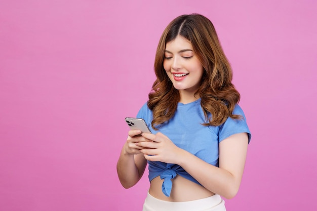 Portret van een gelukkig lachende jonge vrouw die een casual t-shirt draagt met een smartphone die over een roze achtergrond wordt geïsoleerd