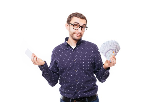 Portret van een gelukkig lachende man in een bril die een hoop geldbankbiljetten vasthoudt en een creditcard toont die over een witte muur wordt geïsoleerd