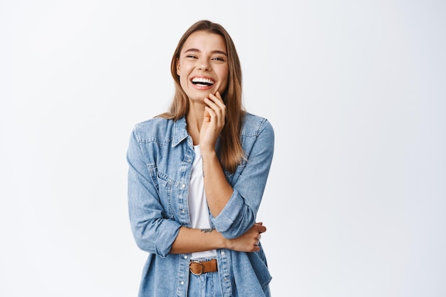 Portret van een gelukkige blonde vrouw in vrijetijdskleding, lachend en plezier makend, vrolijk lachend, staande op wit