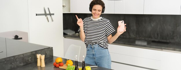 Gratis foto portret van een gelukkige dansende vrouw die voedsel kookt in de keuken en naar muziek luistert in draadloze koptelefoon