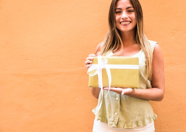 Portret van een gelukkige gift van de vrouwenholding tegen oranje achtergrond