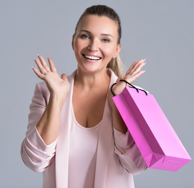 Portret van een gelukkige glimlachende verrassingsvrouw met roze boodschappentas.