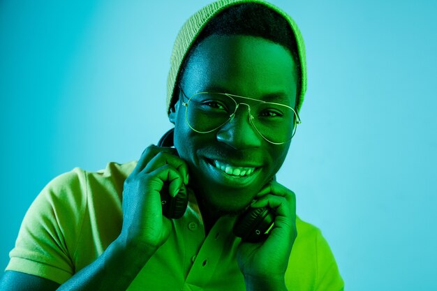 Portret van een gelukkige jonge Afro-Amerikaanse man glimlachend tegen zwarte neon studio achtergrond close-up