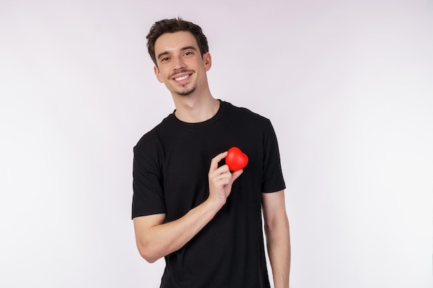 Portret van een gelukkige jonge blanke man met een zwart T-shirt houdt een rode appel vast op een geïsoleerde achtergrond