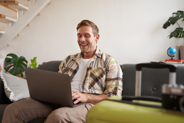 Portret van een gelukkige jonge toerist die zijn vakantie boekt bij een reisbureau en naar een laptop kijkt