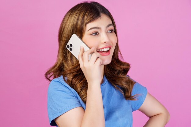 Portret van een gelukkige jonge vrouw die een casual t-shirt draagt en op een mobiele telefoon praat die over roze achtergrond wordt geïsoleerd