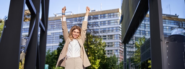 Gratis foto portret van een gelukkige jonge zakenvrouw die de handen opheft, de vuistpomp viert de overwinning en wint iets