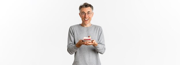 Portret van een gelukkige knappe man van middelbare leeftijd met een bril en een grijze trui die cake vasthoudt en kijkt