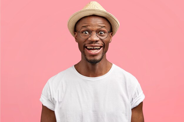 Portret van een gelukkige man van middelbare leeftijd met een gezonde huid, gekleed in een casual wit t-shirt en strooien hoed, geïsoleerd over roze muur