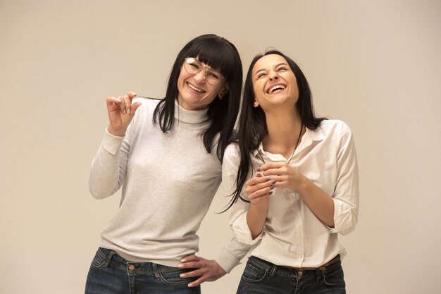 portret van een gelukkige moeder en dochter in de studio op een grijze achtergrond. Menselijke positieve emoties en gezichtsuitdrukkingen concept