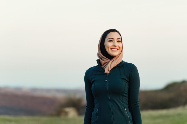 Portret van een gelukkige sportvrouw die in de natuur staat en wegkijkt