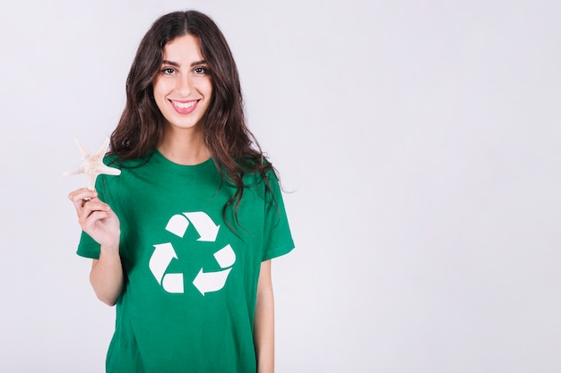 Portret van een gelukkige vrouw in groene t-shirt die overzeese shell houdt