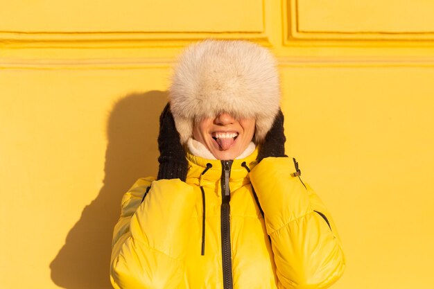 Portret van een gelukkige vrouw met een glimlach in sneeuwwitte zabas in de winter tegen een gele muur op een zonnige dag in een warme Russische Siberische hoed