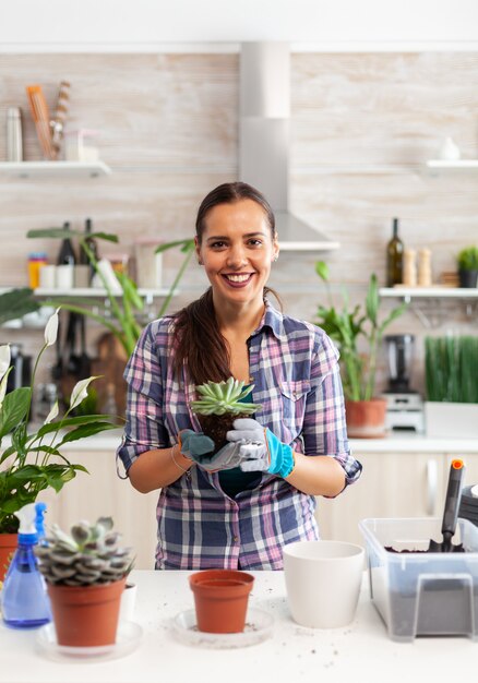 Portret van een gelukkige vrouw met een vetplant die op de tafel in de keuken zit