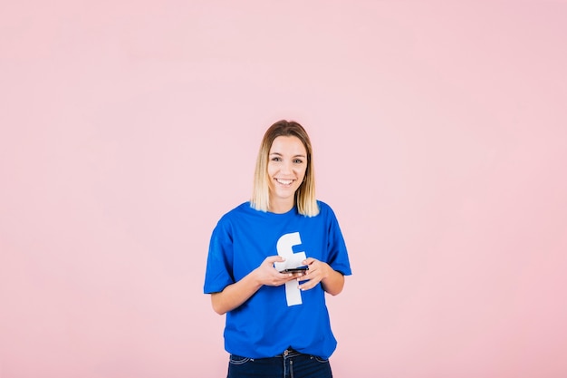 Portret van een gelukkige vrouw met facebook t-shirt met behulp van de mobiele telefoon