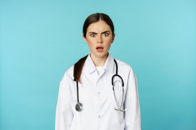 Portret van een geschokte vrouw arts vrouwelijke ziekenhuisstagiair in witte jas die bezorgd en verward kijkt...
