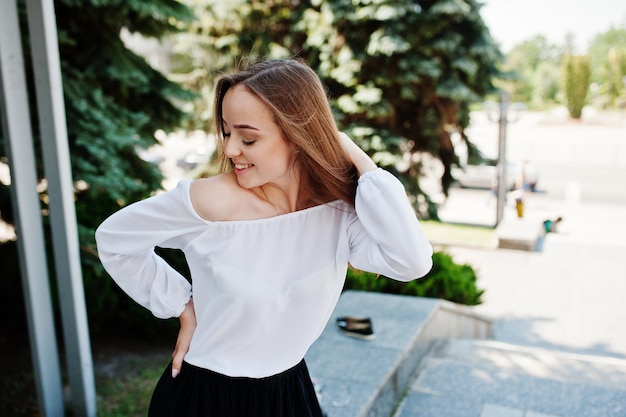 Portret van een geweldige vrouw in witte blouse en wijde zwarte broek poseren met pijnbomen op de achtergrond