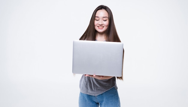 Portret van een glimlachende Aziatische laptop van de vrouwenholding die op grijze muur wordt geïsoleerd