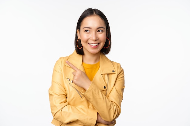 Portret van een glimlachende aziatische vrouw die naar links wijst en een item kiest met een logo of banner op een witte achtergrond