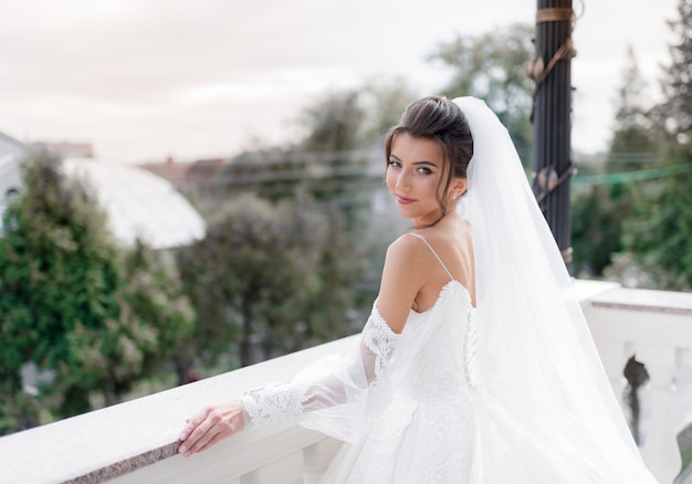 Portret van een glimlachende brunette Kaukasische jonge bruid op het balkon die recht op zoek is