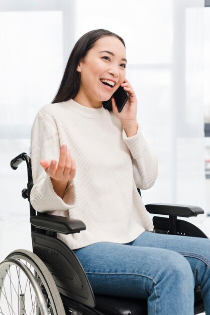 Portret van een glimlachende gehandicapte jonge vrouwenzitting op rolstoel die bij het mobiele telefoon ophalen spreken