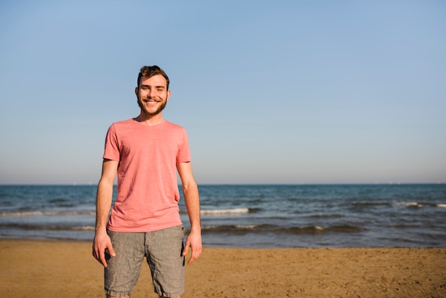 Portret van een glimlachende jonge mens die zich op het strand tegen blauwe hemel bevindt