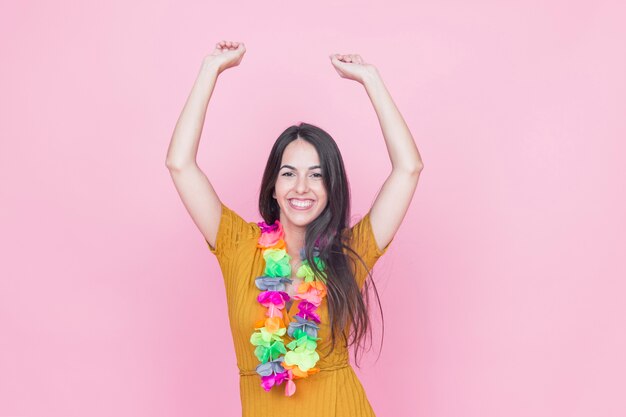 Portret van een glimlachende jonge vrouw die haar wapens op roze achtergrond opheft