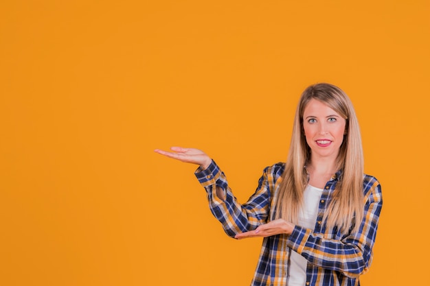 Portret van een glimlachende jonge vrouw die iets voorstelt tegen een oranje achtergrond