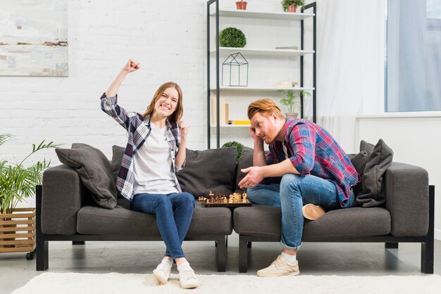 Portret van een glimlachende jonge vrouw die na het winnen van het schaakspel in de woonkamer toejuichen