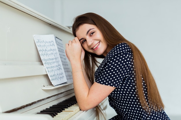 Portret van een glimlachende jonge vrouw die op de piano leunt die aan camera kijkt