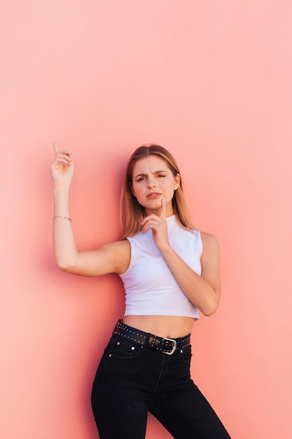 Portret van een glimlachende jonge vrouw met vinger op haar kin wijzende vinger tegen perzik achtergrond