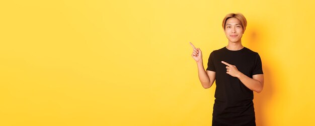 Portret van een glimlachende knappe aziatische man in een zwart t-shirt wijzende vingers in de linkerbovenhoek met lo