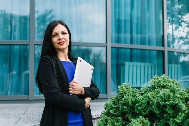 Portret van een glimlachende laptop van de onderneemsterholding voor de glasbouw