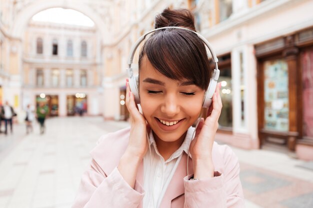 Portret van een glimlachende leuke jonge vrouw het luisteren muziek met oortelefoons