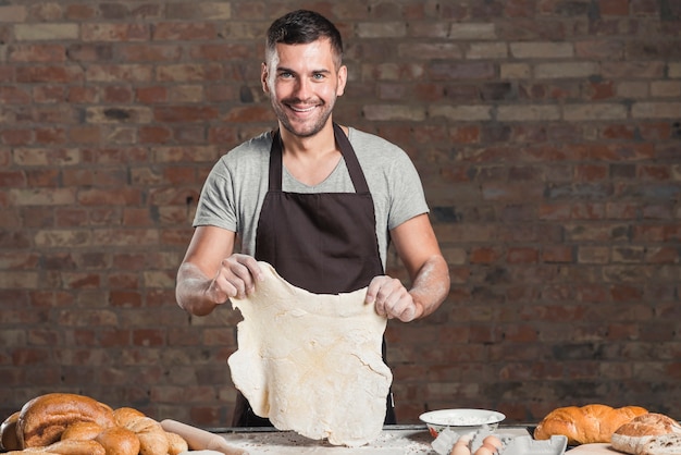 Gratis foto portret van een glimlachende mannelijke bakker die brood in bakkerij voorbereiden