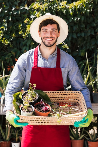 Portret van een glimlachende mannelijke tuinman die ingemaakte installaties in de mand houden